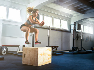 Fitness woman jumping on box training at the gym, crossfit exercise
