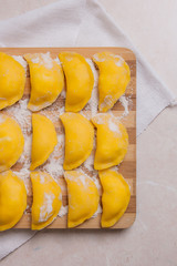 Ready for boiling vareniki, dumplings, pierogi on wooden cutting board with flour and wooden rolling pin, sieve ..