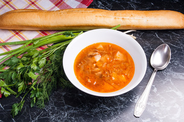 Vegetables and meat in red beetroot soup or borsch in white plate on dark marble background.