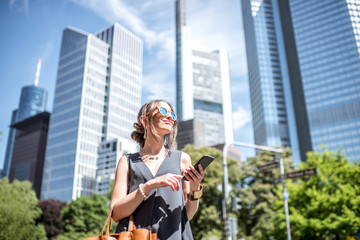 Lifestyle portrait of a businesswoman with phone and bag in the modern district in Frankfurt city - obrazy, fototapety, plakaty
