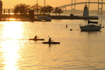Two kayakers are out i the evening water, near the Newport Pell Bridge in Newport, Rhode Island
