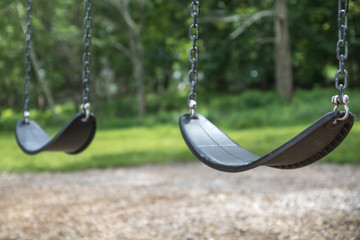 Swings at an outside playground. The swing set is black rubber with metal chain. It is the swing...