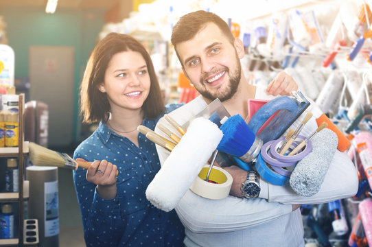 Young Friendly Couple Demonstrating Tools For House Renovating In Paint Store