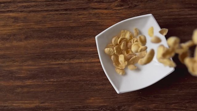 Corn flakes falling in white bowl with copyspace to the left on wooden table.
