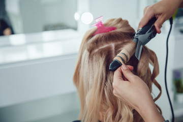 Fototapeta premium Hair stylist makes a curls for a girl, using hair styling. Hairdresser at work.