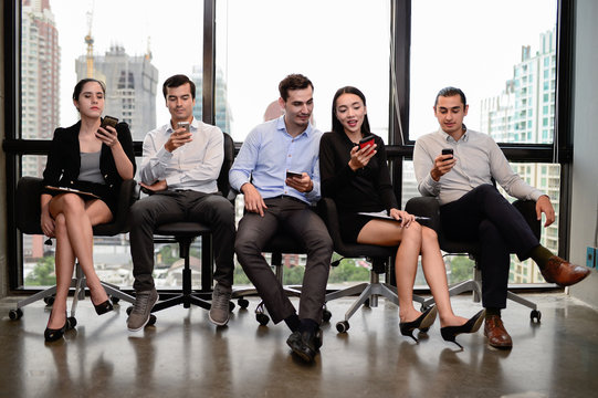three businessman and two businesswoman relax sit on chair and hold phone at window in the office