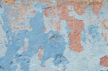 An old concrete wall with peeling blue and red paint. Vintage texture.