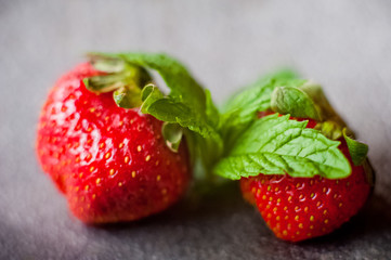 A beautiful ripe fresh strawberry with refreshing mint and sweet powdered sugar on the background of a concrete lid
