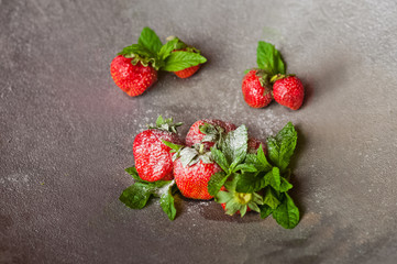 A beautiful ripe fresh strawberry with refreshing mint and sweet powdered sugar on the background of a concrete lid