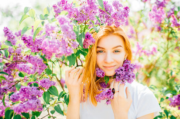 Obraz na płótnie Canvas Portrait of young attractive cute redhair girl outdoor in park in blooming lilac bushes in summer sunny day. Resting among paradise flowers. Fragrance and fresh smell. Tenderness, innocence, airness.