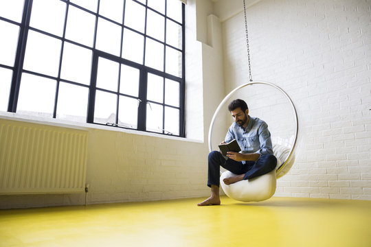 Young man sitting on swing in his loft reading a book