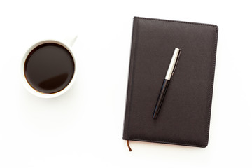 a Cup of black coffee and a day planner with pen on white background. Flat lay minimal business concept of working place in the office.