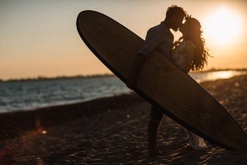 Happy surfers couple standing with surfboards on the sandy beach