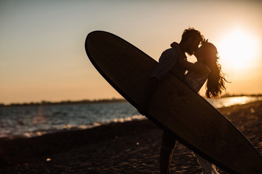 Happy surfers couple standing with surfboards on the sandy beach