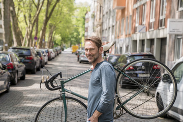 Fototapeta na wymiar Portrait of smiling mature man carrying his bicycle on the shoulder