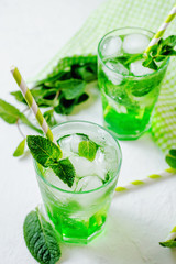 Green alcoholic or non-alcoholic refreshing summer cocktail, mojito, sparkling drink with mint and ice in a traditional glass on a white rustic background 