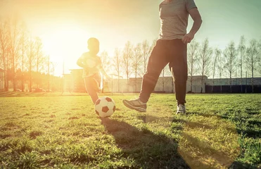 Outdoor kussens Father and son playing together with ball in football under sun © Andrii IURLOV