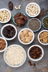 Above view of ingredients for homemade granola, oats, different nuts and raisins, dates, seed on the grey stone background, selective focus