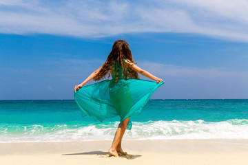 Young beautiful girl in blue dress on the beach of a tropical island. Summer vacation concept.