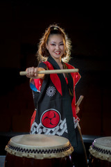 Fototapeta premium beautiful asian taiko drummer girl in red with drumsticks, studio shot on a dark background.