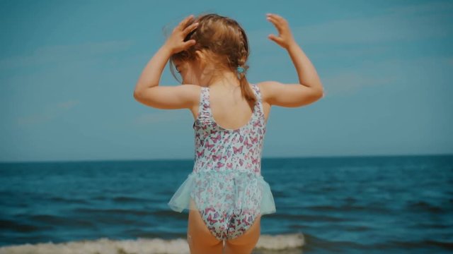 small and adorable little girl runs on a beach by the sea in summer