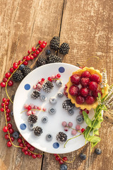 Various berries of blackberries, currants, blueberries are covered with frost on a plate and sprigs of mint. And a cake with berries. Soft sun natural light.
