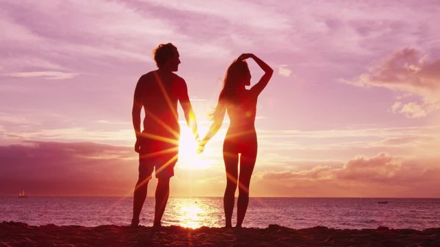 Romantic couple holding hands on beach at sunset with amazing light and colors. Young fit couple on honeymoon enjoying travel vacation summer holidays on beach. SLOW MOTION RED EPIC.
