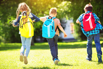 Children with rucksacks standing in the park near school. Pupils with books and backpacks outdoors