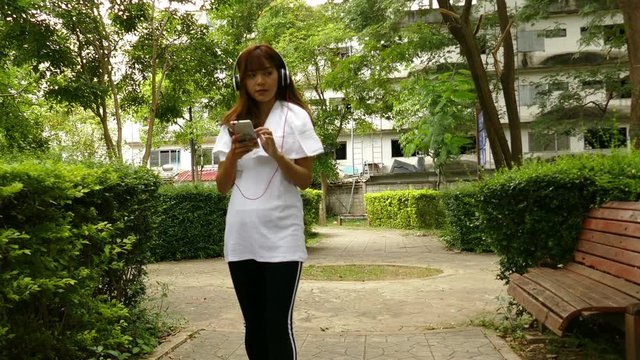 asian woman with headphones. young female  holding mobile smart phone. beautiful girl listening to music in public park