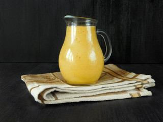 Yellow fruit juice in a glass jug standing on a towel on a black background