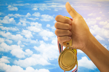 Fototapeta na wymiar winner hand raised and holding gold medals against blue sky. success award concept