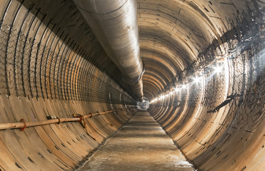 Empty underground tunnel under construction for the metro. Large temporary ventilation pipe under the ceiling. Focus on the center of the frame
