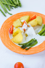 Potatoes and asparagus with tomatoes and tartar sauce on plate ready to eat.