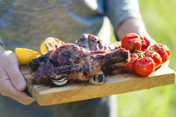 Barbecue veal steaks with cherry tomatoes on cutting board in man hands