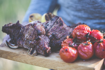 Barbecue veal steaks with cherry tomatoes on cutting board in man hands