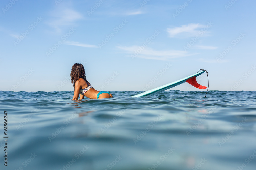 Wall mural Beautiful surfing girl in sexy bikini sit on a front of big longboard surfboard board so we see one single fin of her surf on sunrise or sunset. Modern active sport lifestyle and summer vacation.