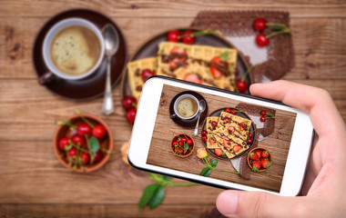 Fototapeta na wymiar Hands taking photo Belgian waffles with berry and cup of coffee with smartphone.