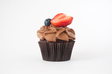 Chocolate cupcake with whipped chocolate cream, decorated fresh strawberry, blueberry on white background. Picture for a menu or a confectionery catalog.