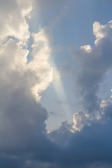 Clouds on blue sky pierced by ray of sunlight, vertical