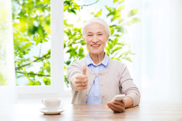 senior woman with smartphone showing thumbs up