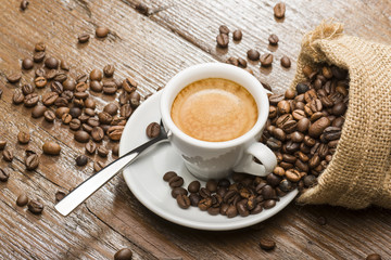 cup of coffee with burlap sack and coffee beans on wooden table.