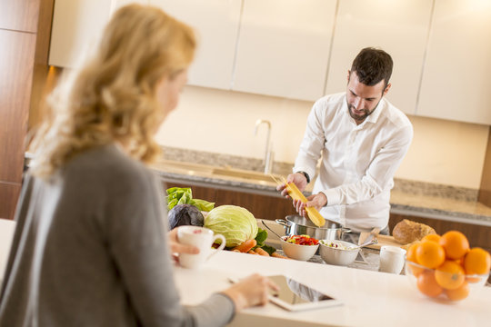 Man preparing a meal while a young woman sitting and use of tablets in a modern kitchen