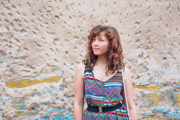 Young woman standing in front of aged stone wall background with rusty, peeling rocks and yellow and blue colors