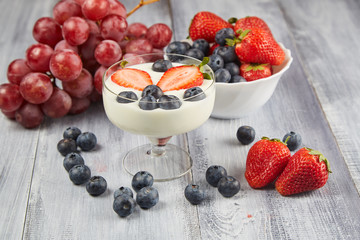 Strawberry, blueberry with yogurt and grapes on a gray wooden background