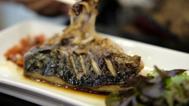 woman's hand eating grilled Mackerel or Saba fish with soy sauce in japanese restaurant