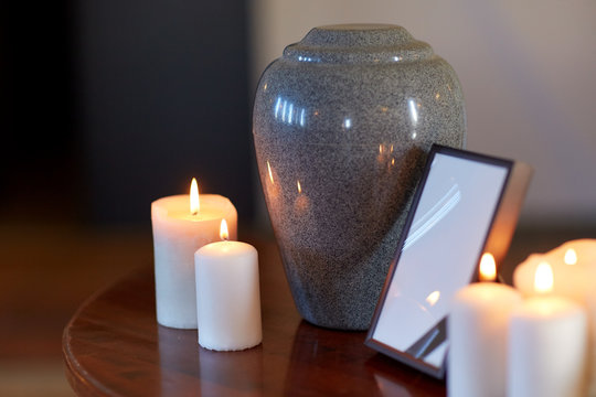 photo frame, cremation urn and candles on table