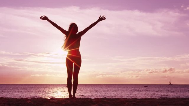 Happiness, freedom and success - Happy serene blissful woman raising arms up at amazing sunset at beach. Young woman enjoying the idyllic serenity. RED EPIC SLOW MOTION.