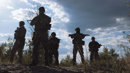 Military force silhouettes standing and posing near tree on battlefield.