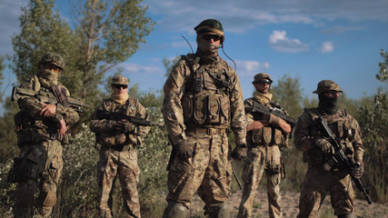 Group of soldiers in a camouflage and the hidden persons with weapon pose and look in the camera
