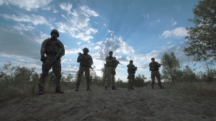 Silhouettes of cool soldiers standing in nature in a row.